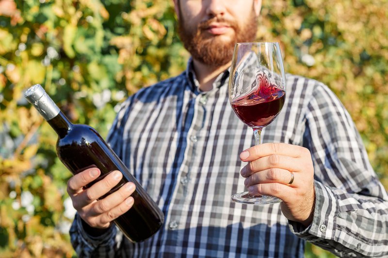 Красивый винодел держит в руке бутылку и бокал красного вина