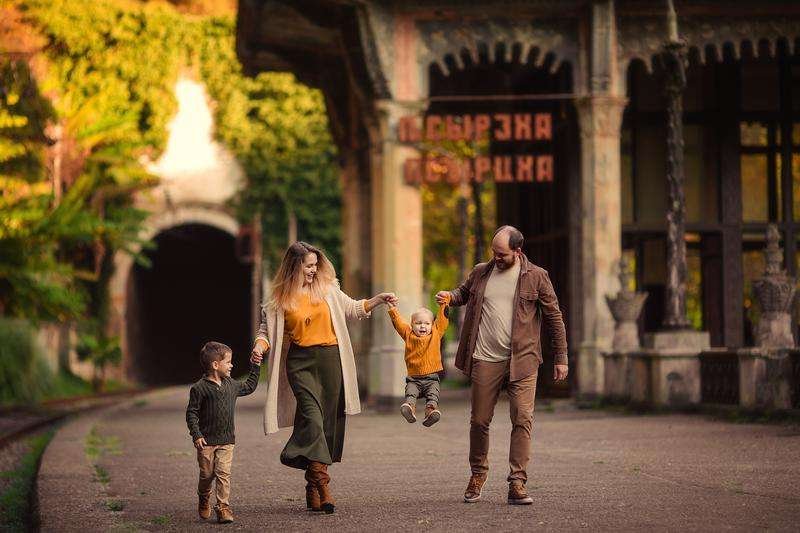 A happy family on a walk in autumn against the backdrop of an abandoned railway station in Abkhazia.