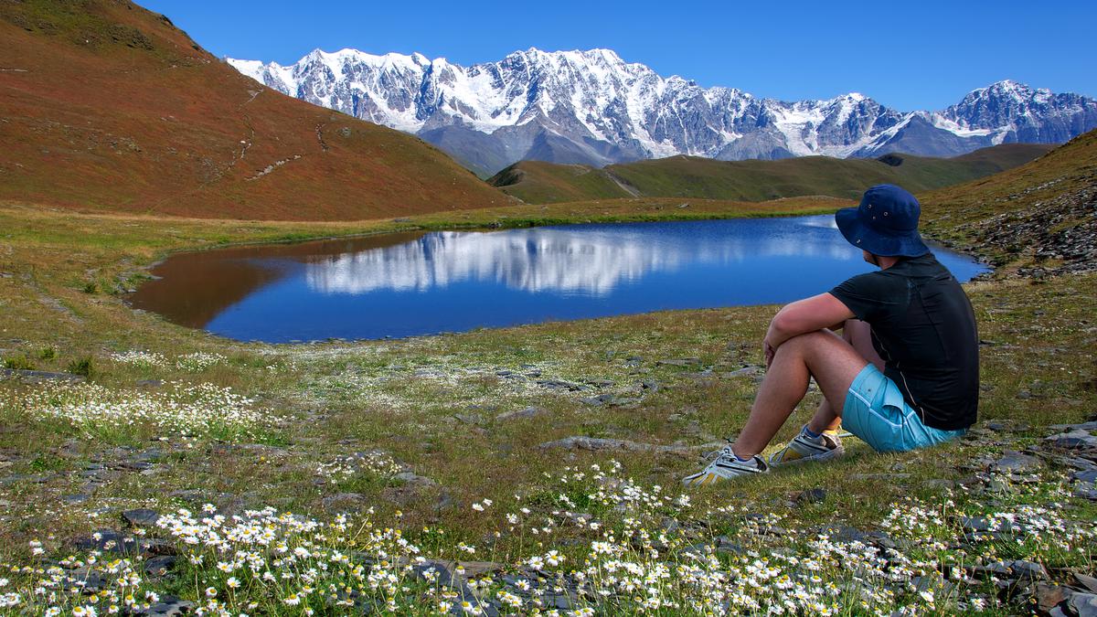 Молодой человек сидит возле озера и смотрит на горы в Сванетии
