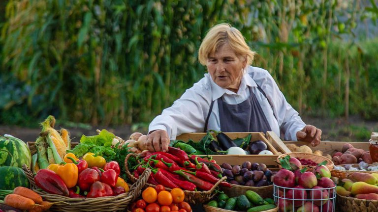 Пожилая женщина раскладывает овощи на прилавке