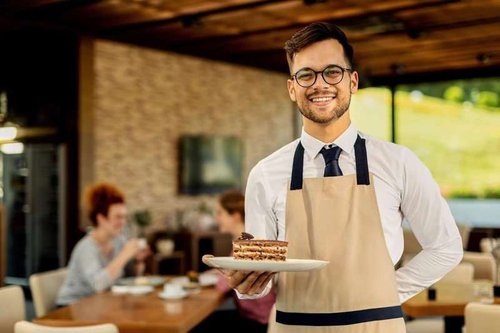 A neat and friendly waiter carries dessert on a plate to a customer
