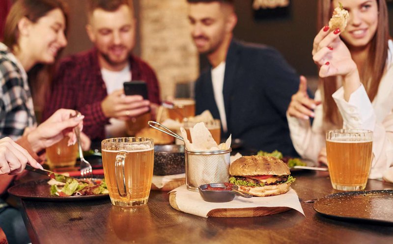 A group of friends are eating burgers and drinking beer