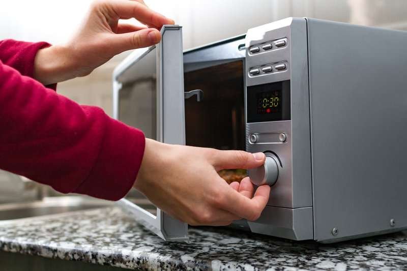 A woman's hand closes a microwave oven.