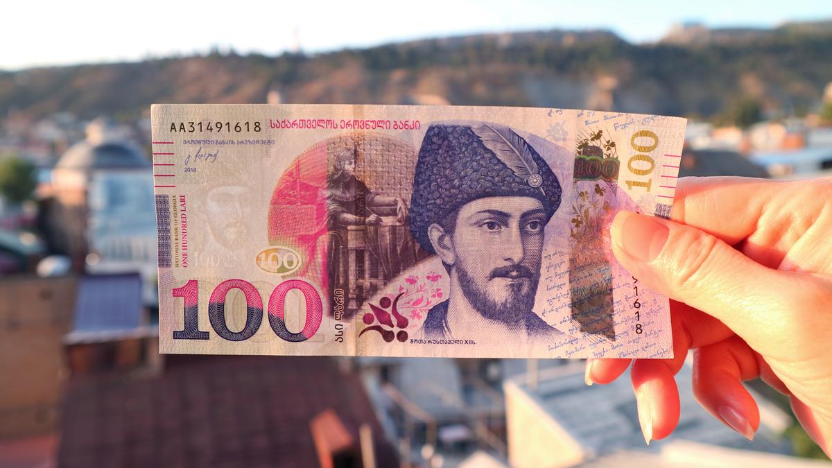 Женская рука держит грузинскую банкноту 100 лари