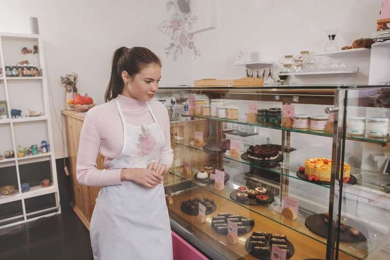 A pastry shop employee looks at a display case with desserts.