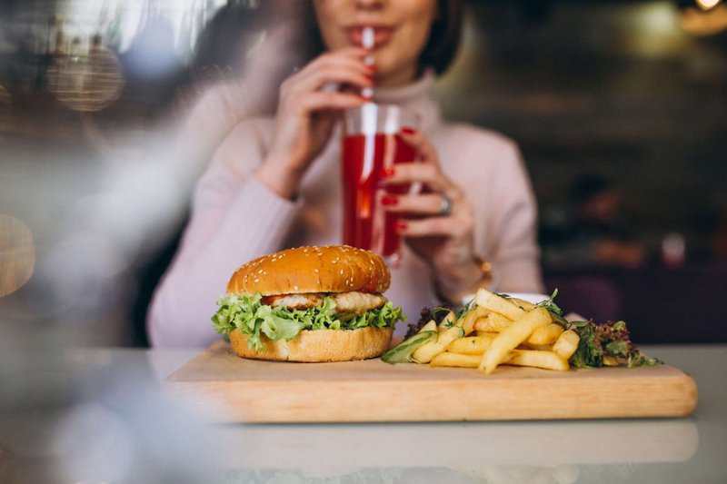A woman with a burger sipping a cocktail