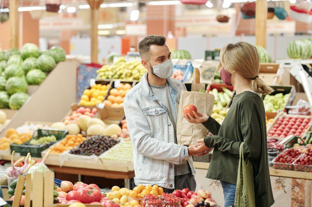 Молодая пара в тканевых масках стоит у прилавка и покупает продукты