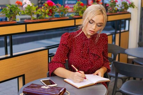 A woman with glasses, dressed in business style, writes down the number of visitors to a location in a notebook
